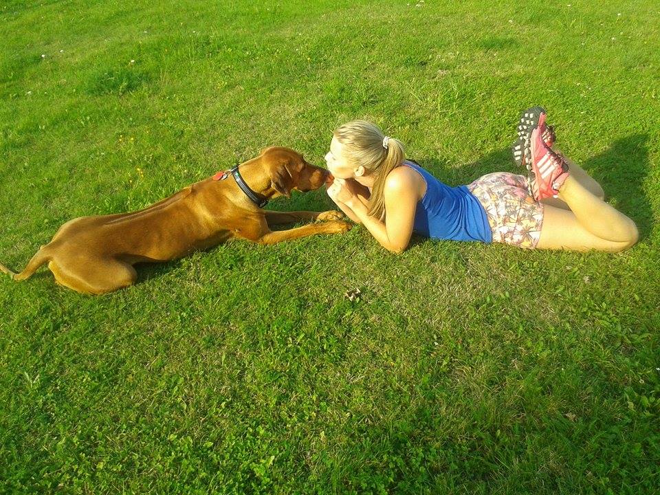 woman laying on grass kissing dog
